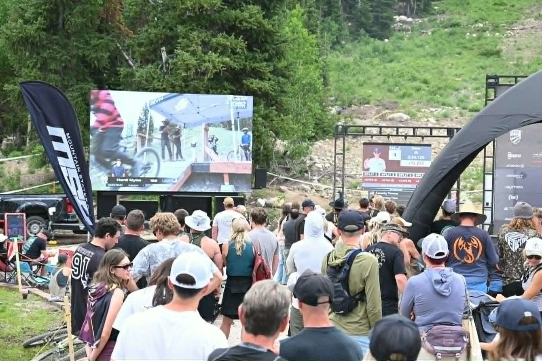 Spectators watching downhill coverage on a large outdoor video wall